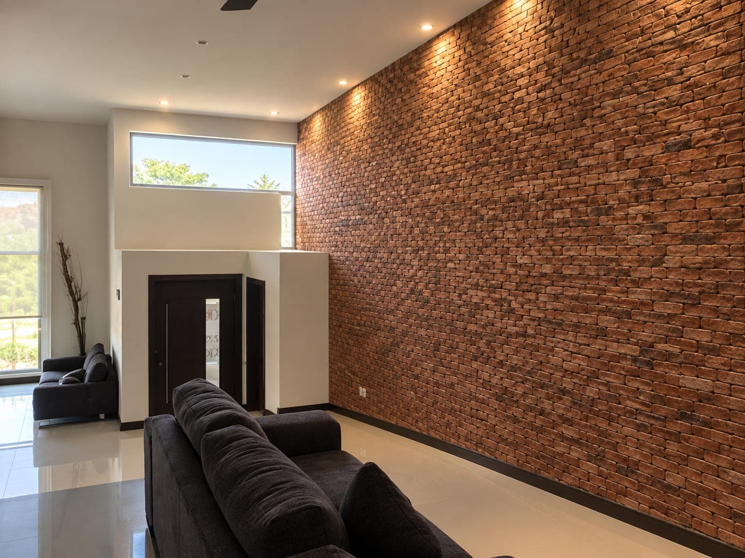 Estancia de doble altura con muro de ladrillo aparente en Casa Armonía