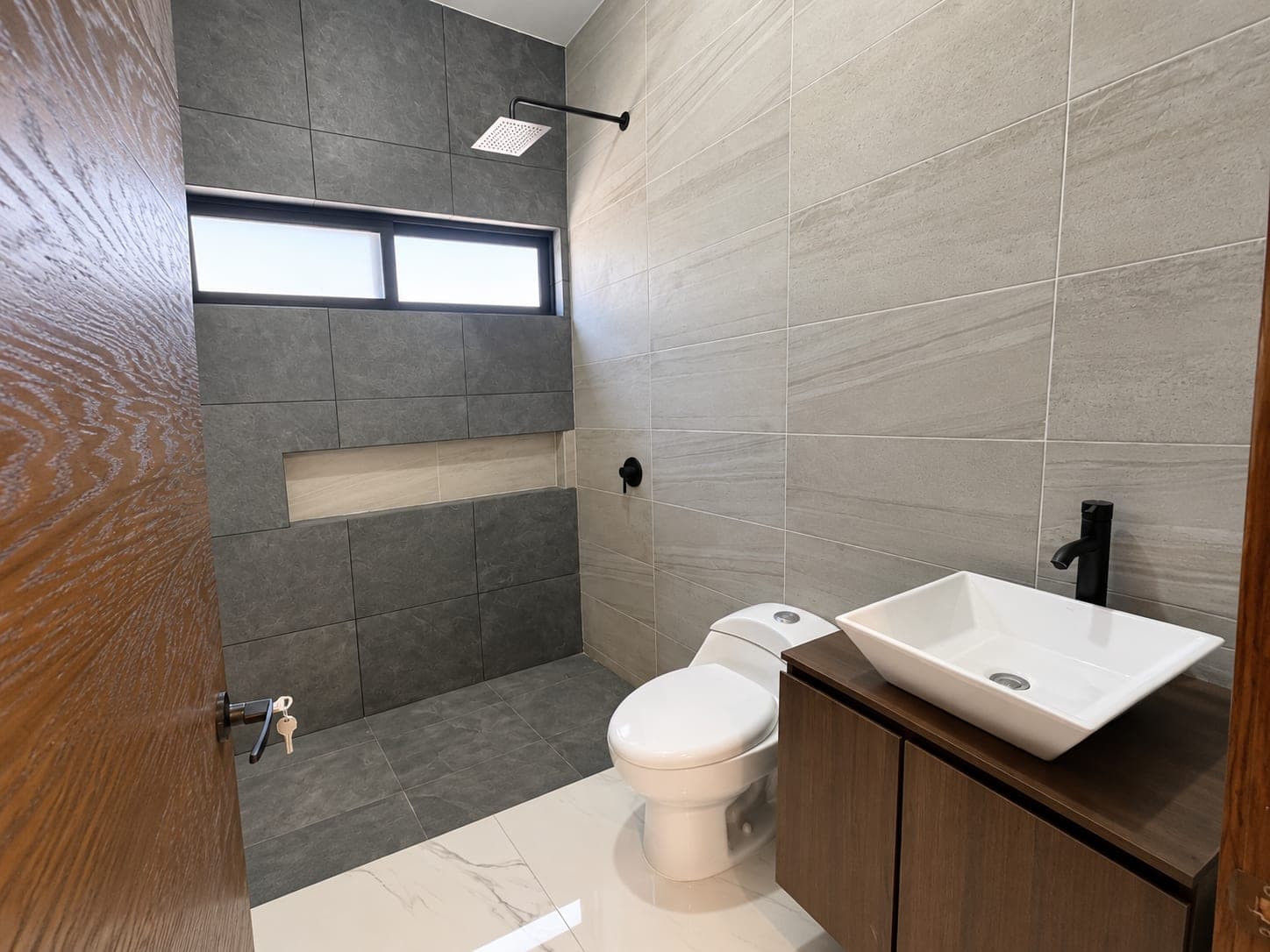 Baño de Casa Aurora con regadera en azulejo oscuro y lavabo sobre mueble de madera