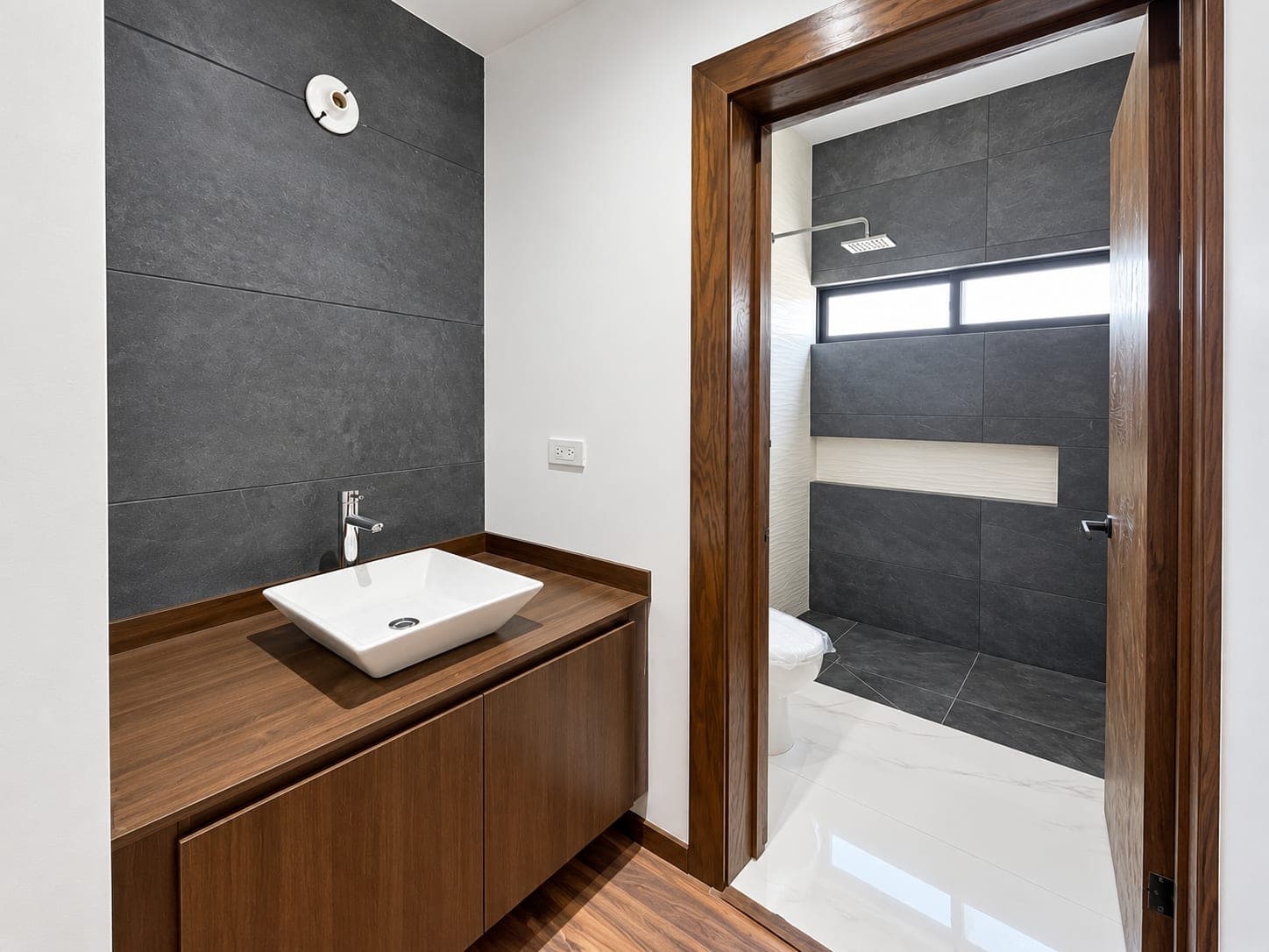 Lavabo de Casa Aurora frente a un muro oscuro, con el baño al fondo