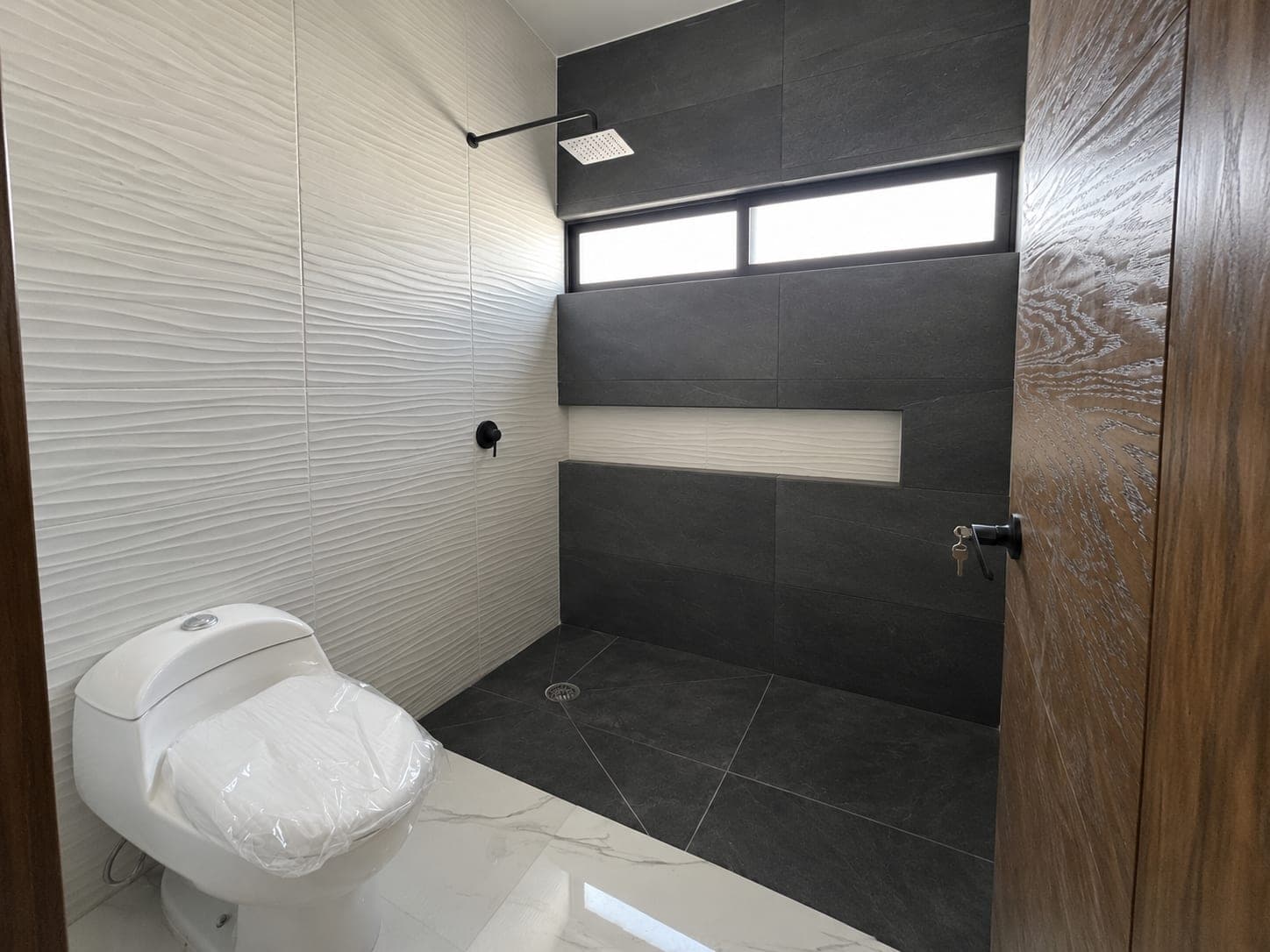 Baño de Casa Aurora con azulejo blanco ondulado y regadera en tono oscuro