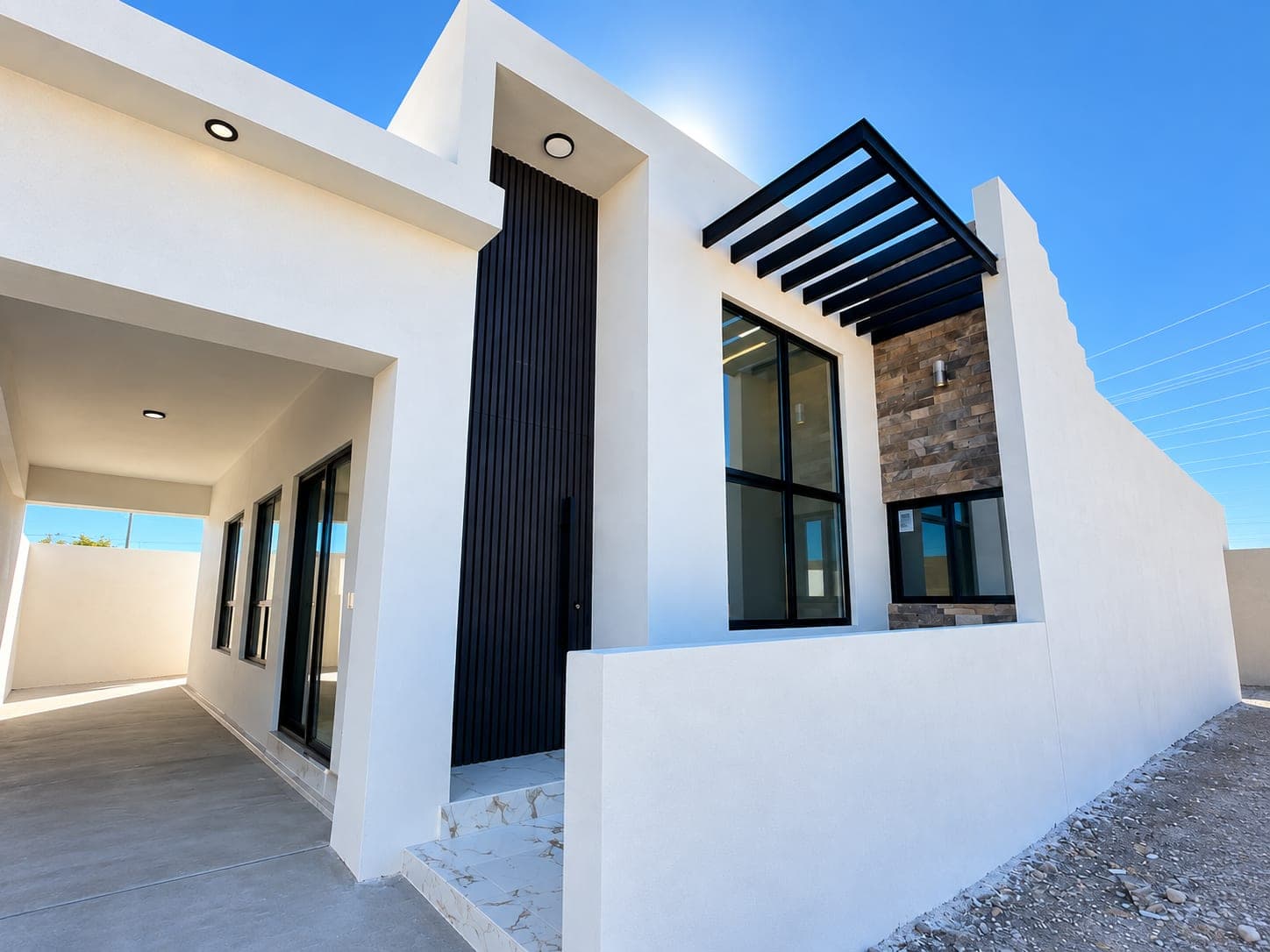 Acceso de Casa Plenitude con puerta de listones negros, pérgola y muro de piedra